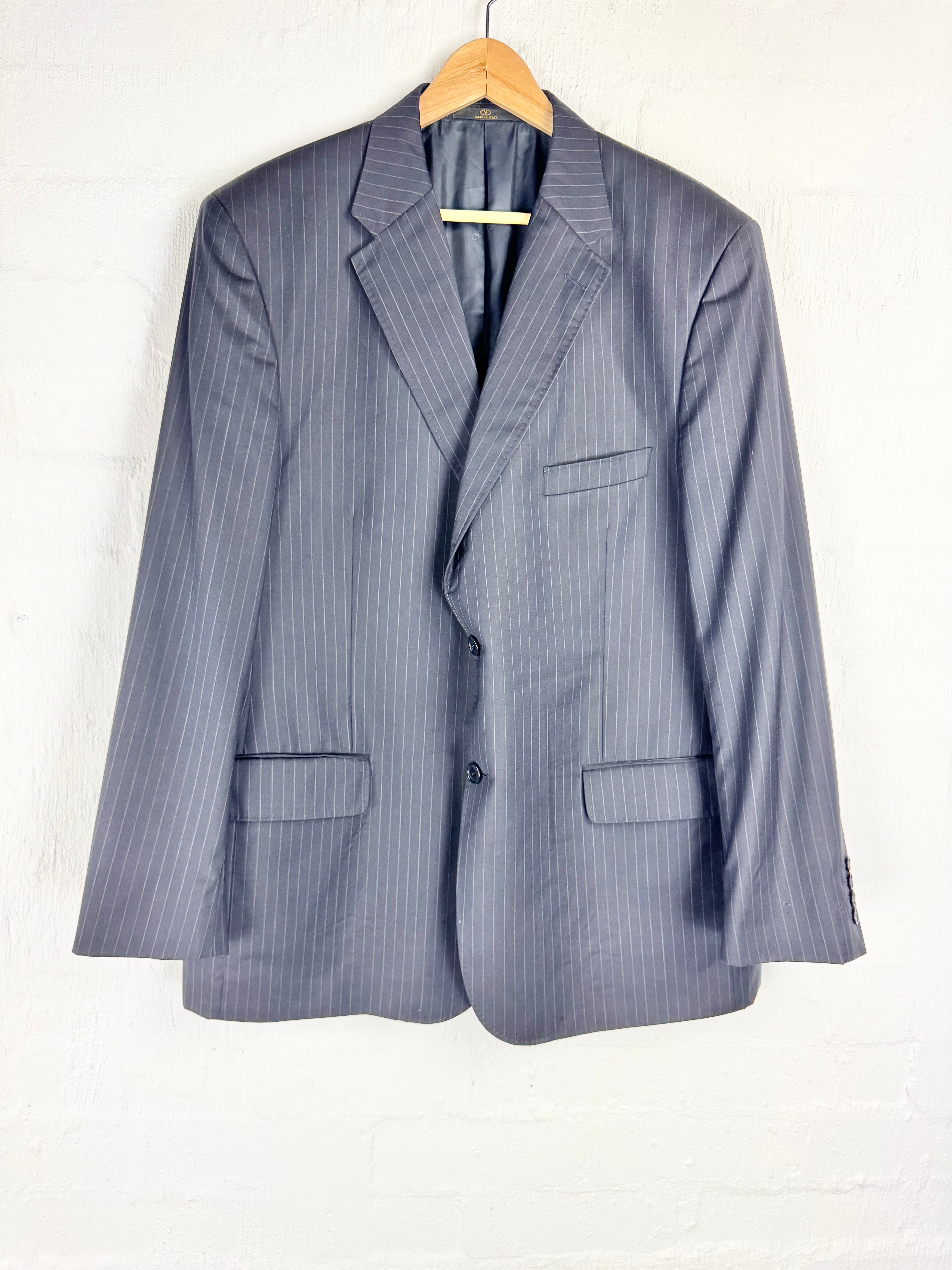 A gray pinstripe blazer jacket hanging on a wooden hanger against a white brick wall.