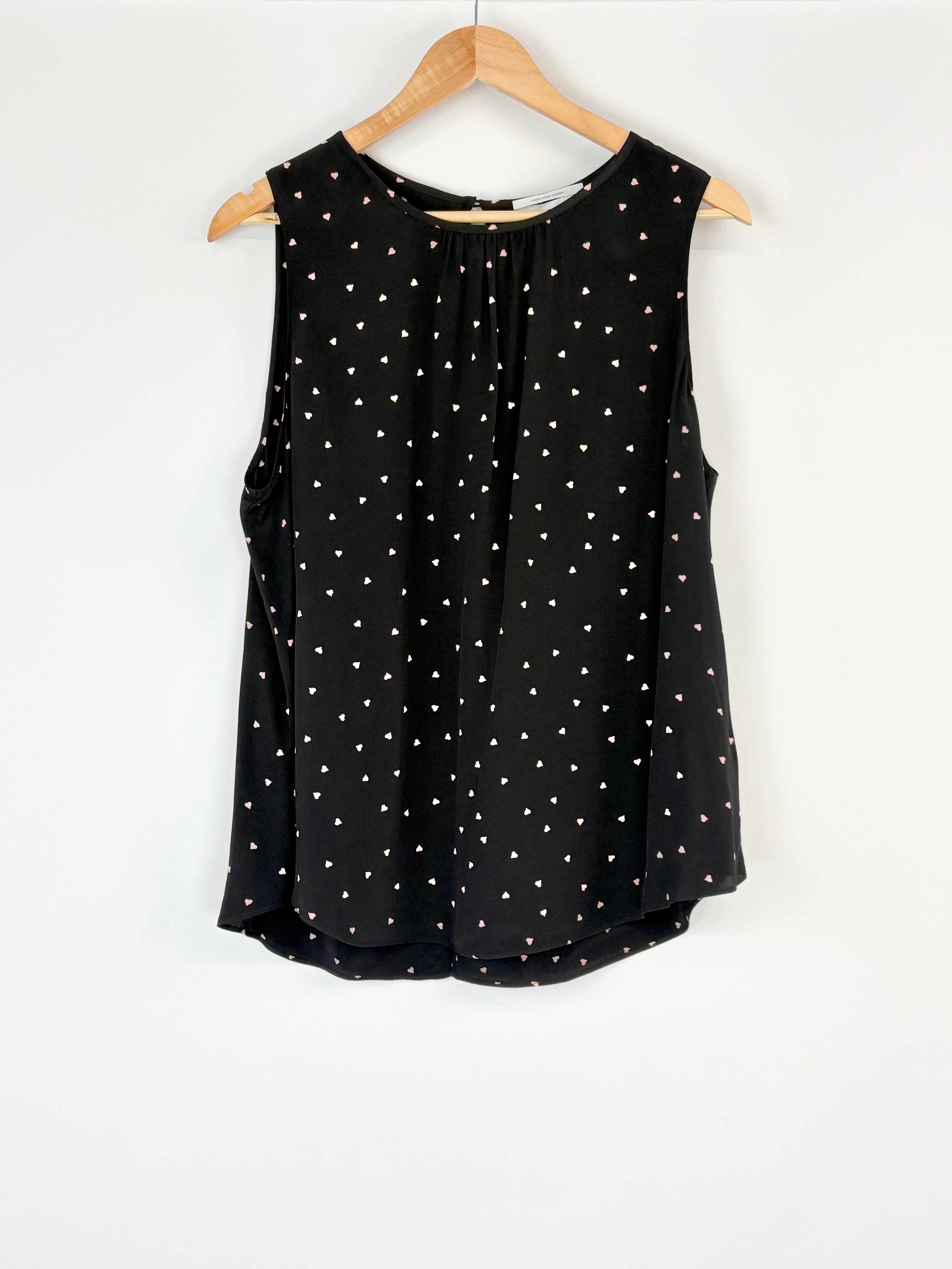Black sleeveless top with white polka dots on a wooden hanger against a white background