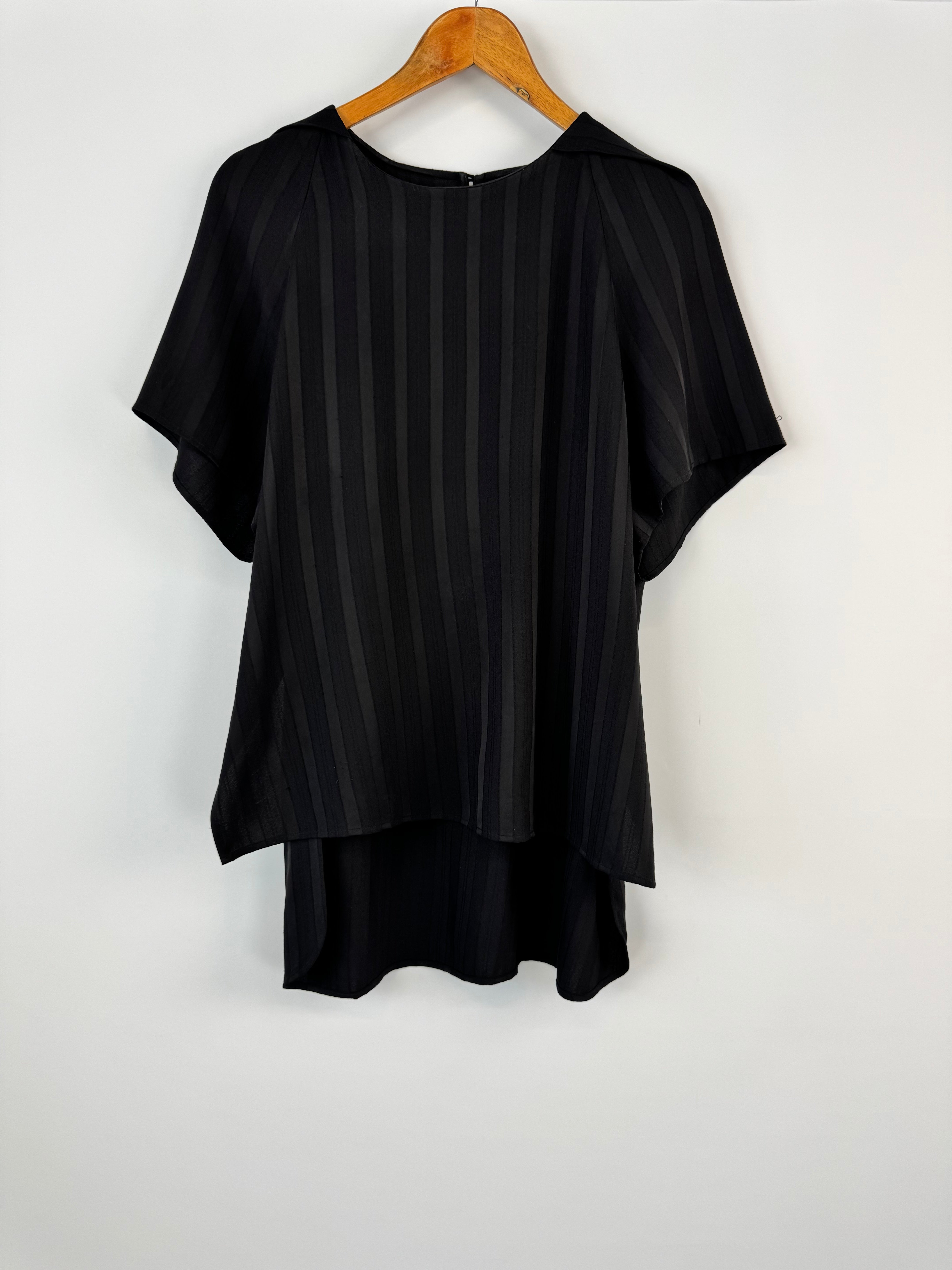 Black pleated top on a wooden hanger against a white background