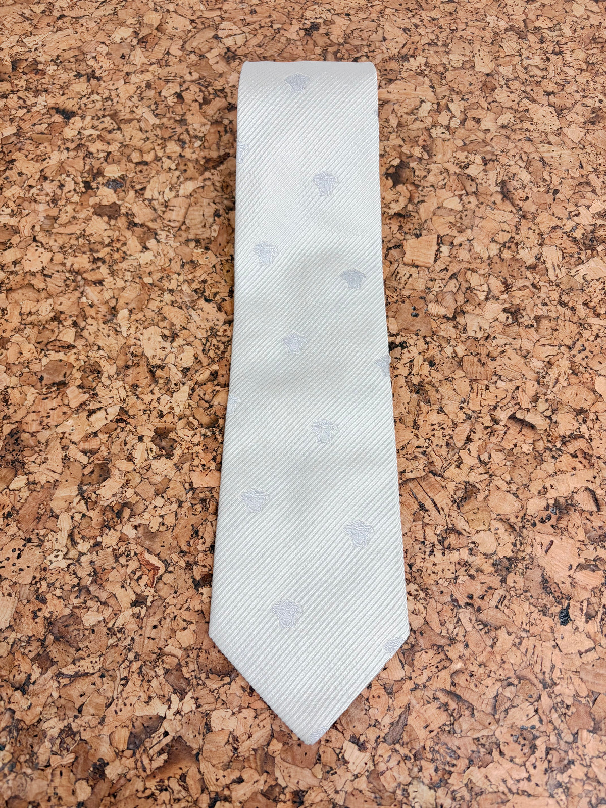 A light gray textured tie with subtle circular patterns, laid flat on a brown cork background.