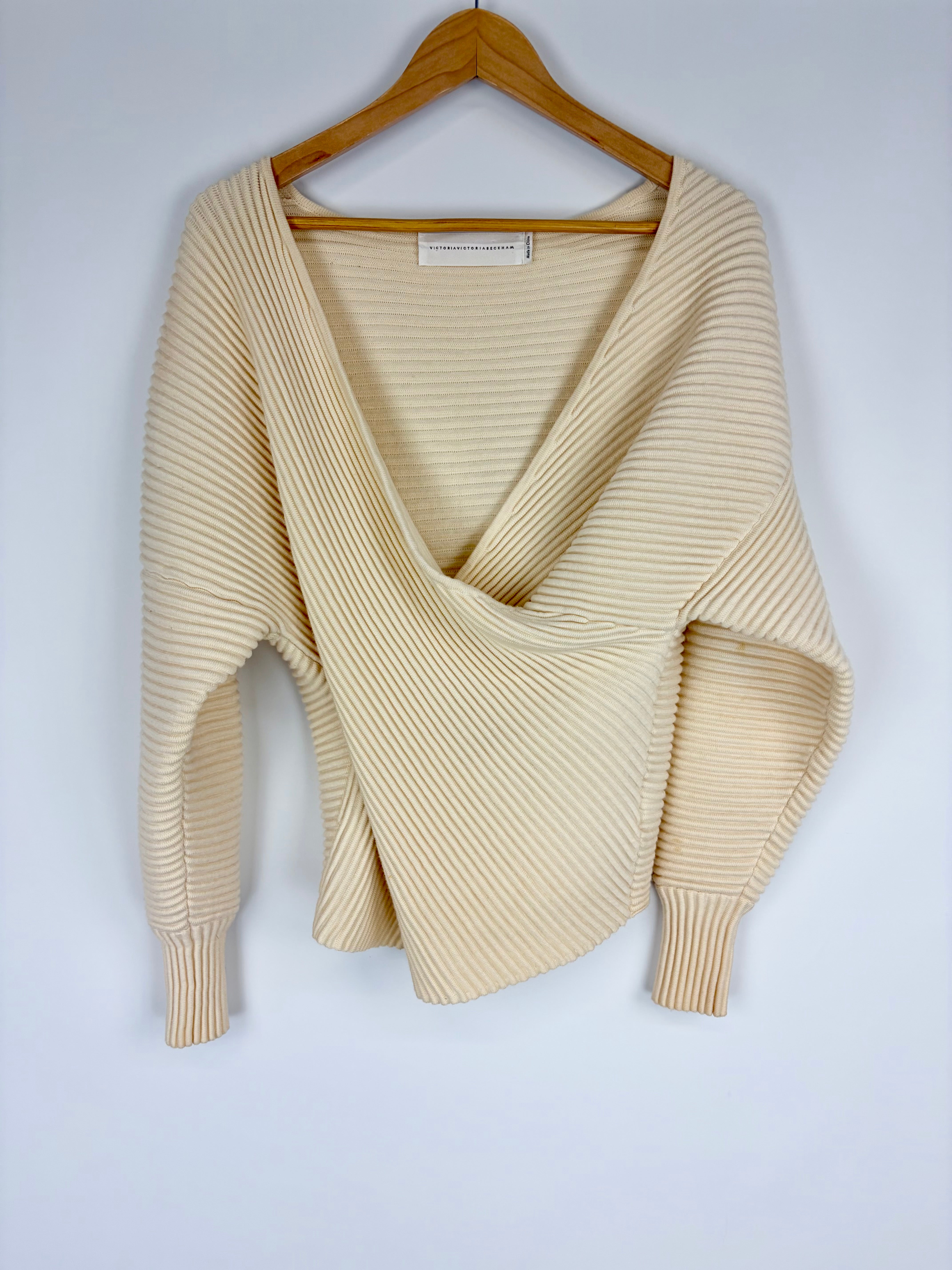 Beige ribbed sweater on a wooden hanger against a white background