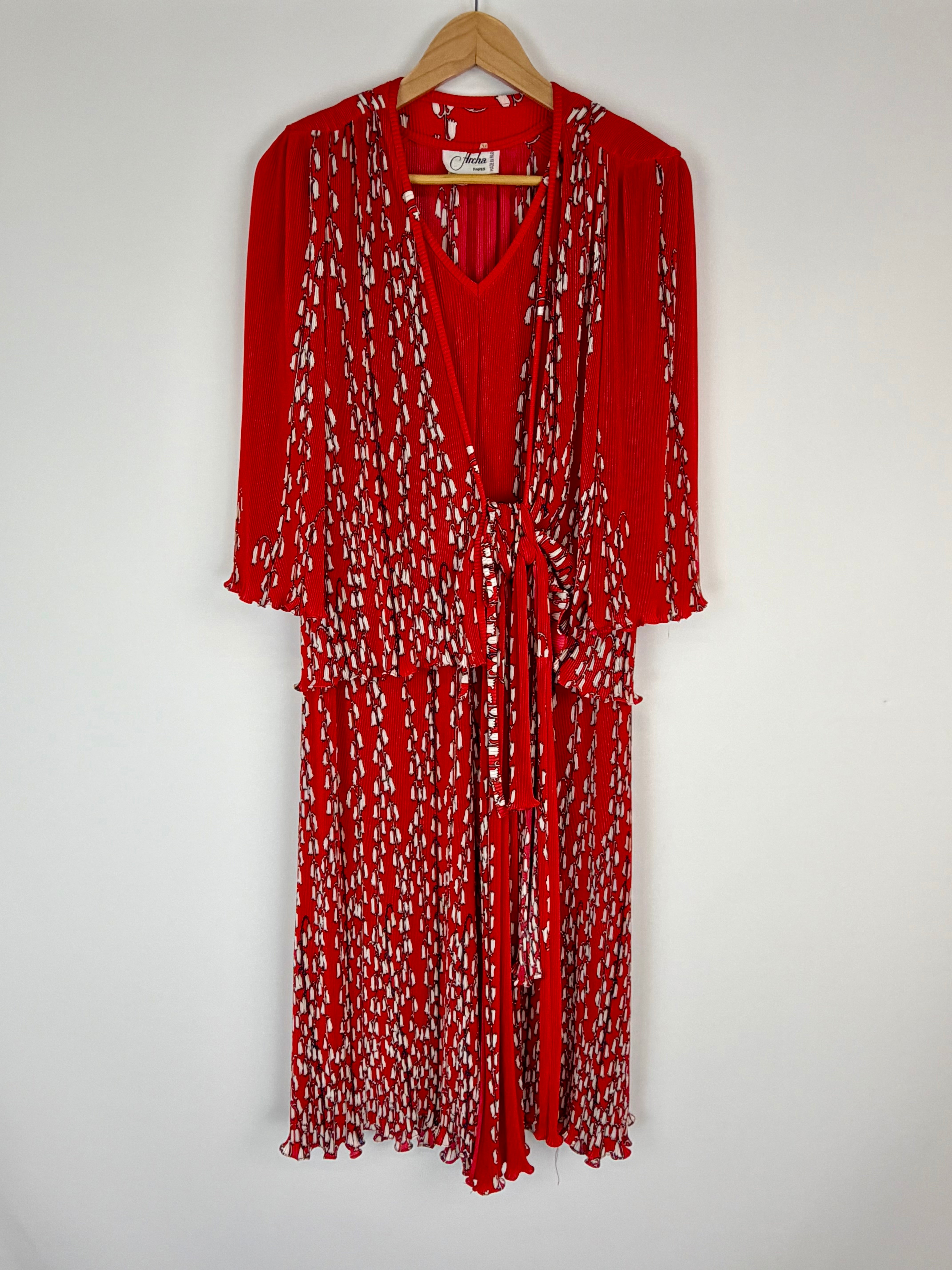 Red dress with white pattern on a hanger against a white background