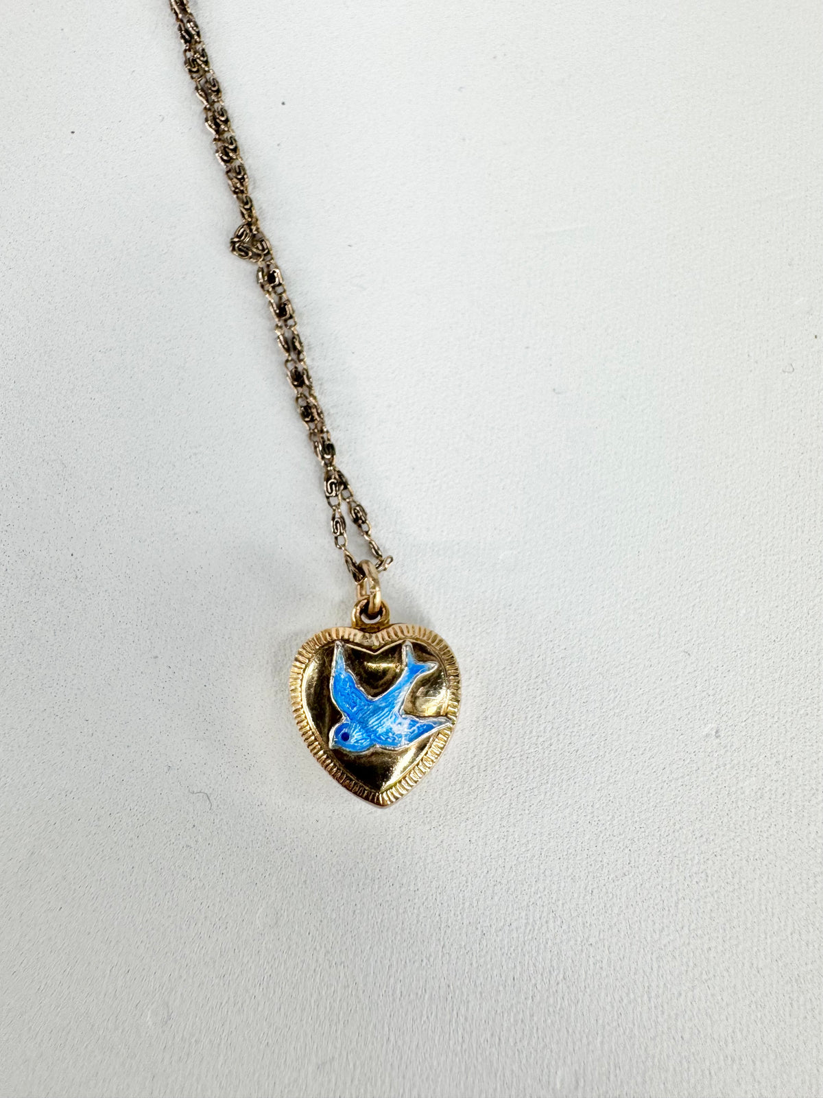 Heart-shaped pendant with blue bird design on a chain against a light gray background