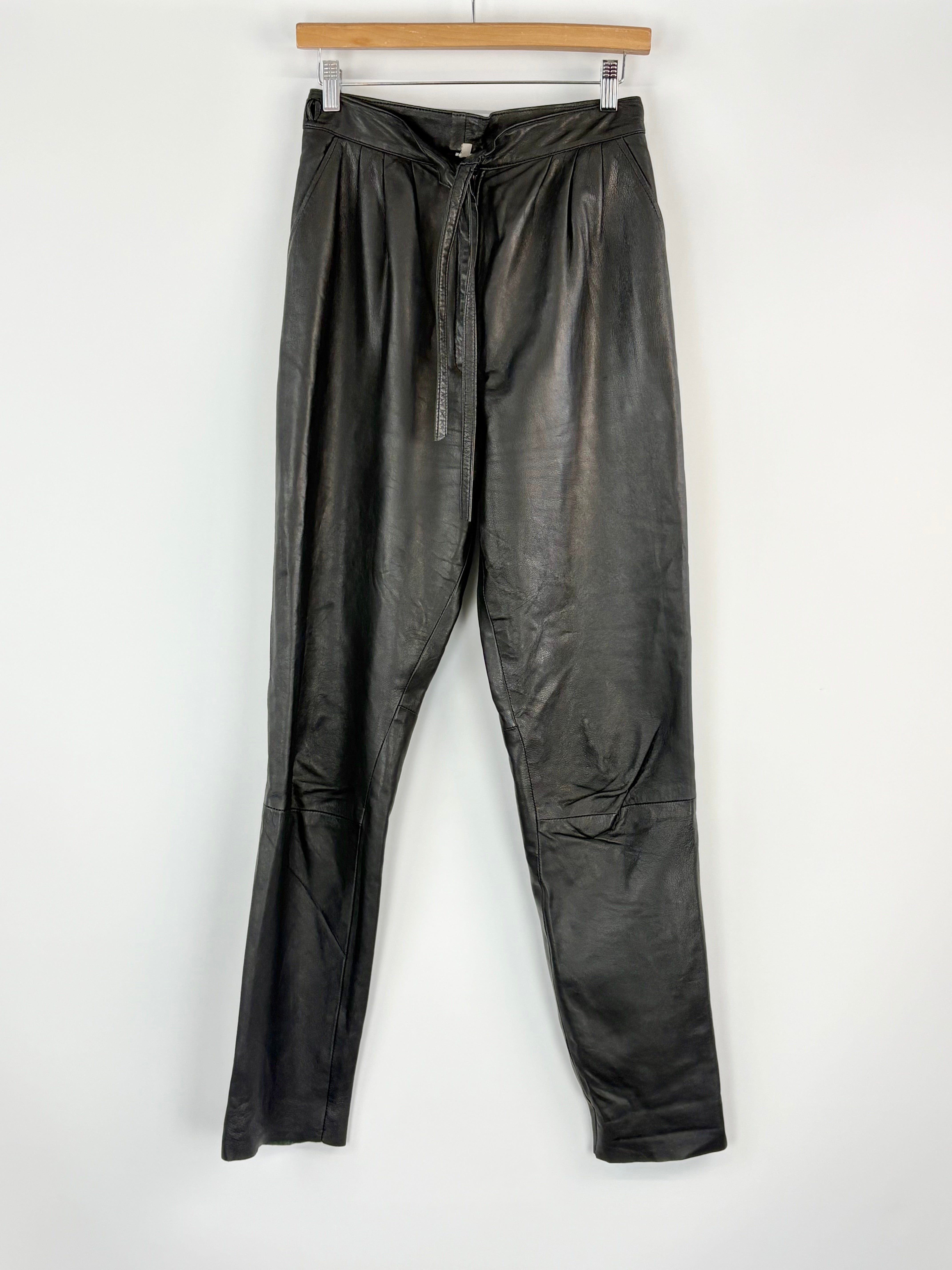 Black leather pants hanging on a wooden hanger against a white background