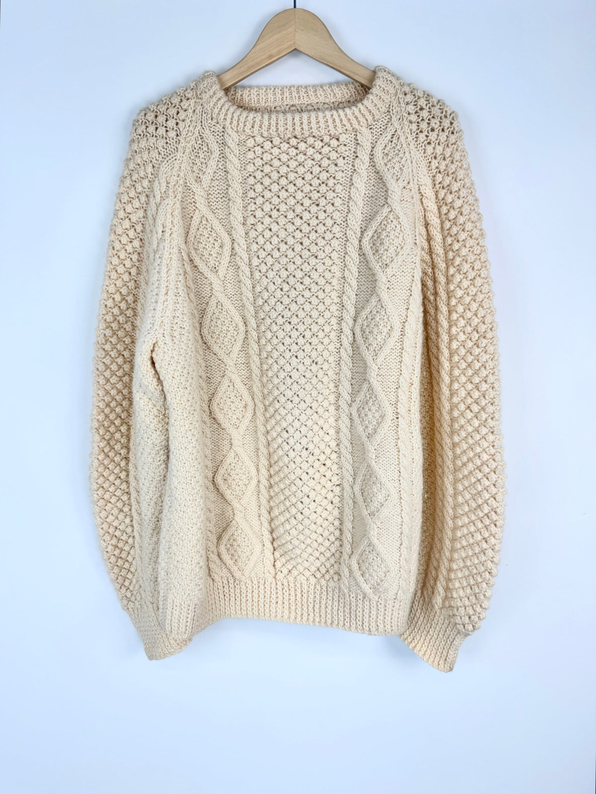 Beige knitted sweater on a wooden hanger against a light blue background