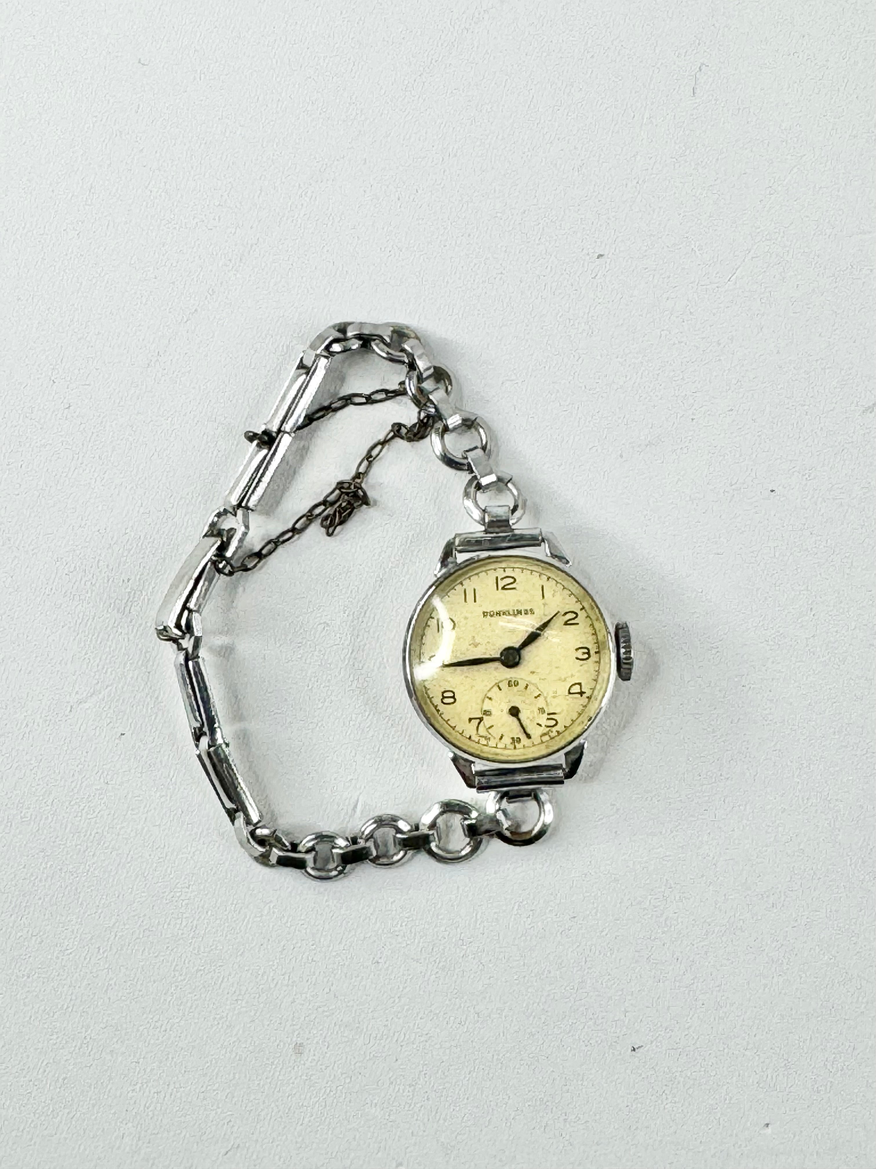 A vintage silver Swiss watch with a metal chain and a round analog dial, not in working condition.