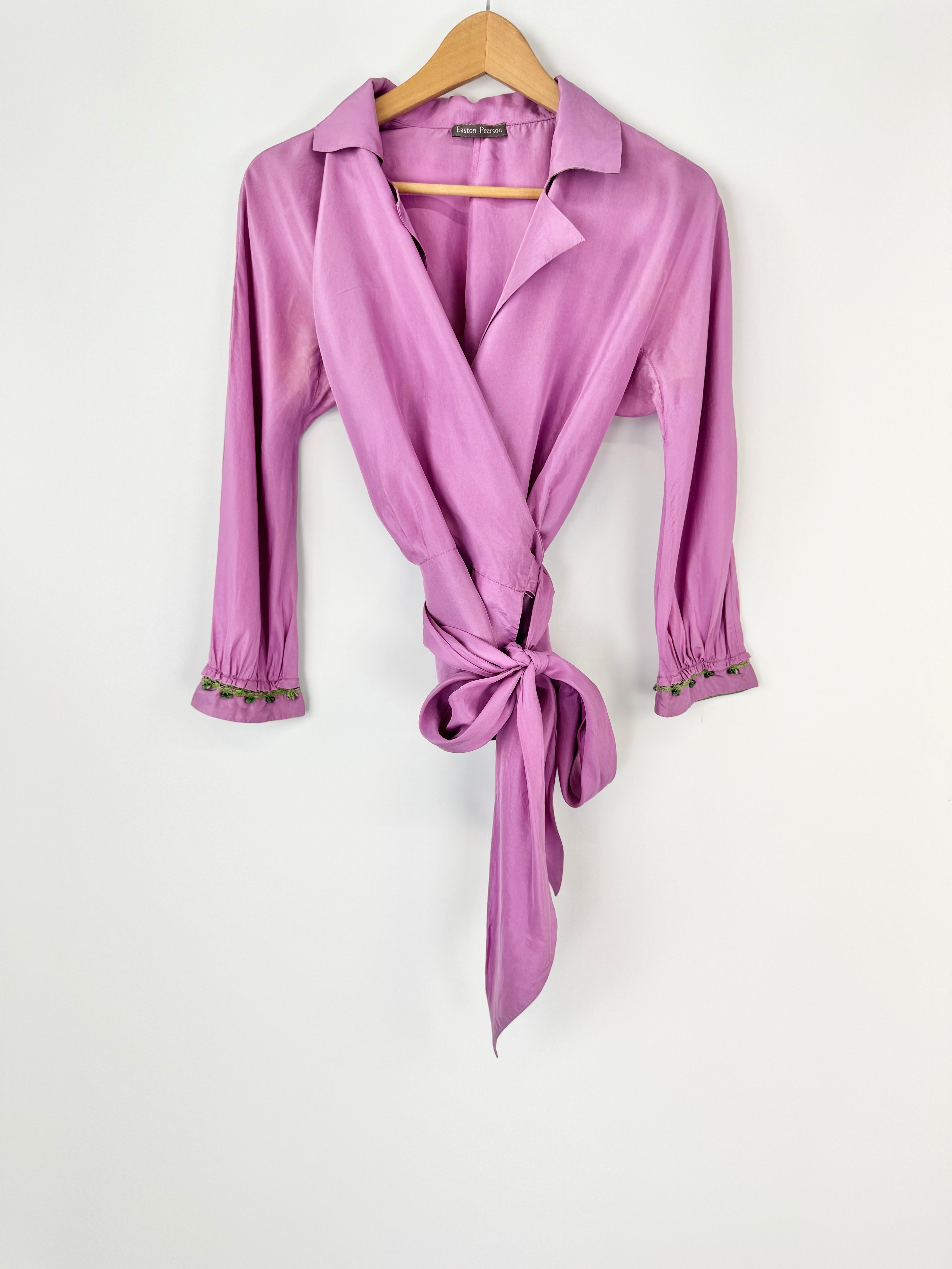 Purple wrap-style blouse on a hanger against a white background