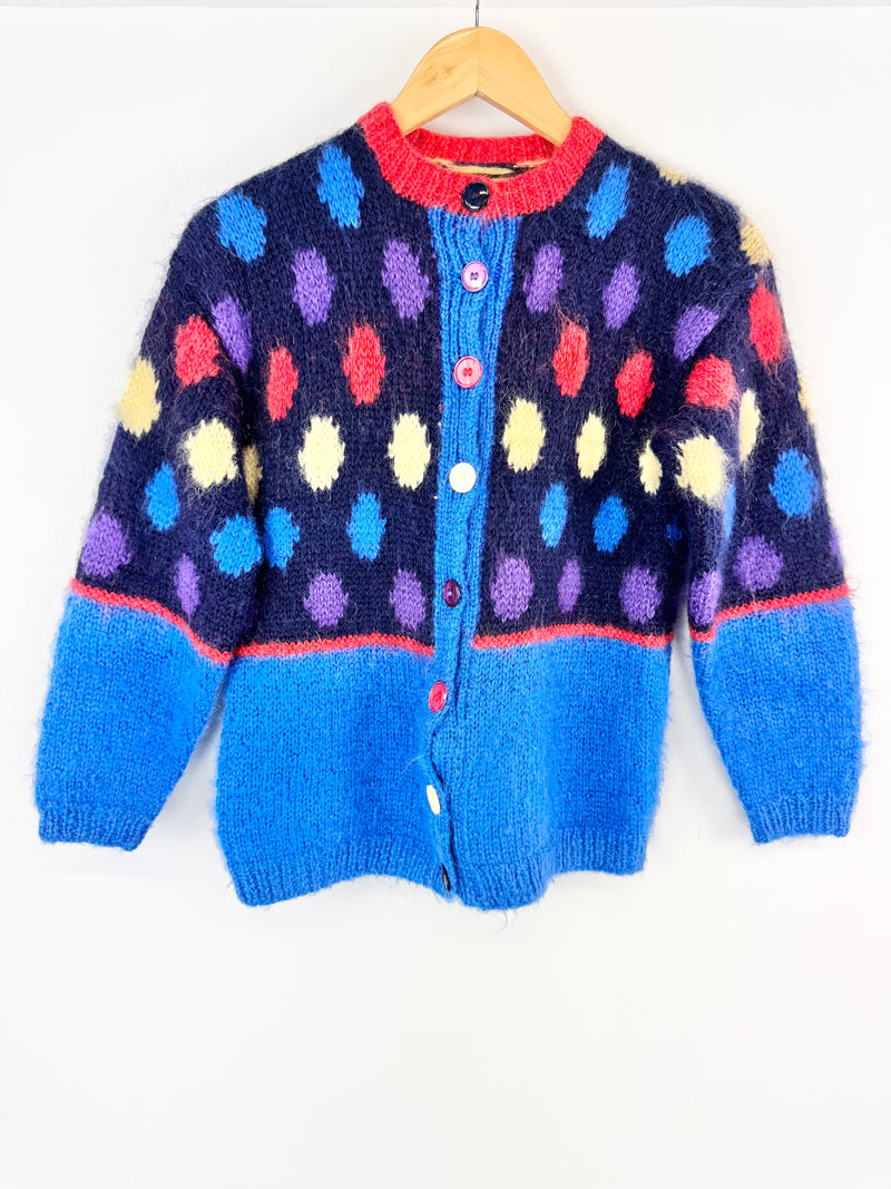 Colorful polka dot cardigan on a hanger against a white background