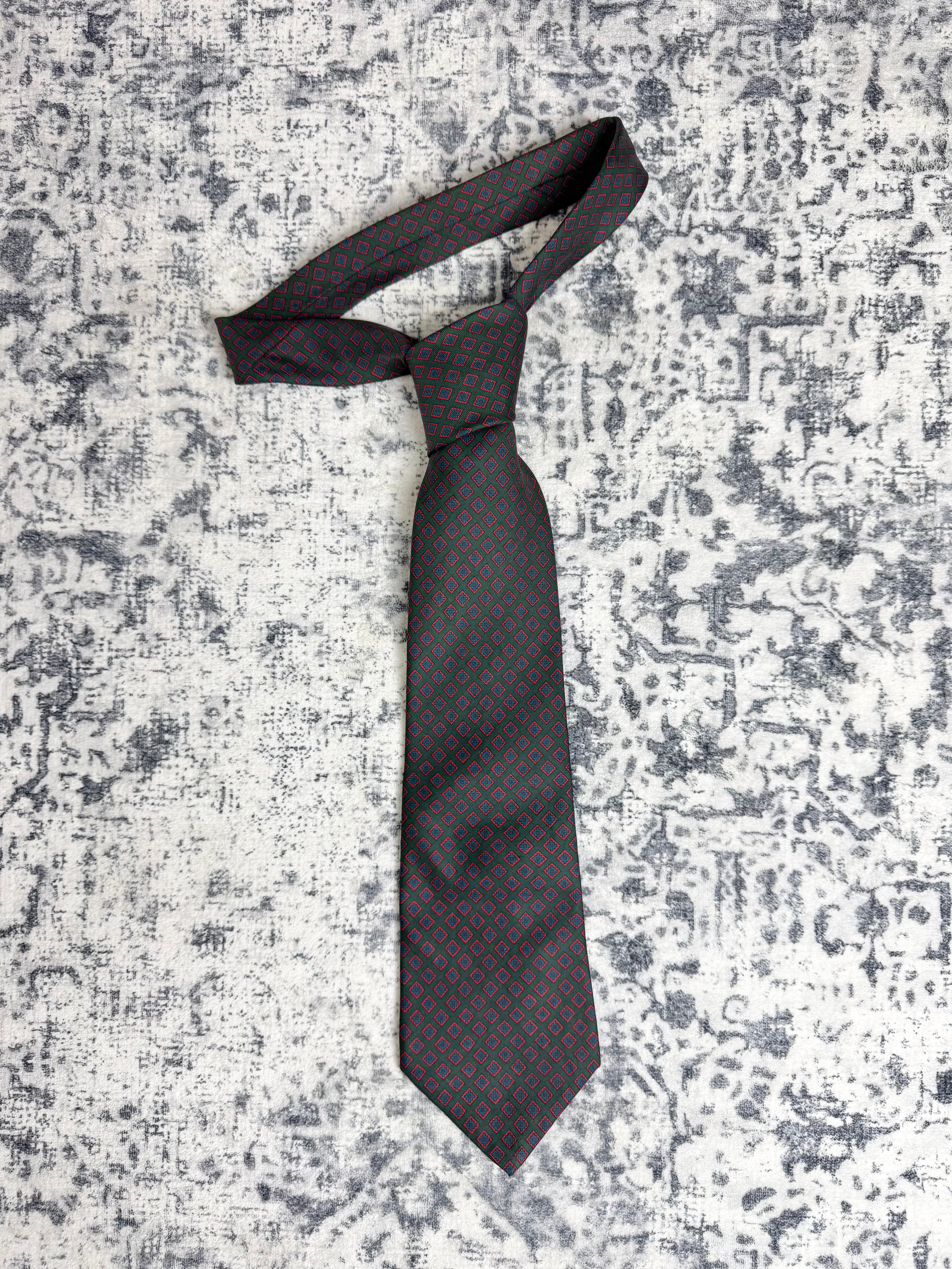A dark gray necktie with a small red geometric pattern, knotted in a standard style and laid flat on a distressed gray and white textured background.