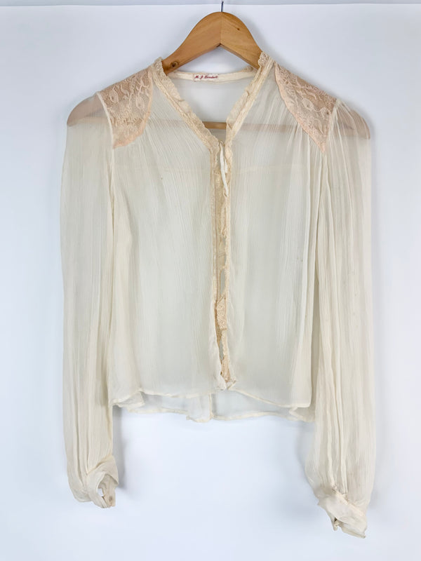 White sheer blouse with lace details on a wooden hanger against a white background