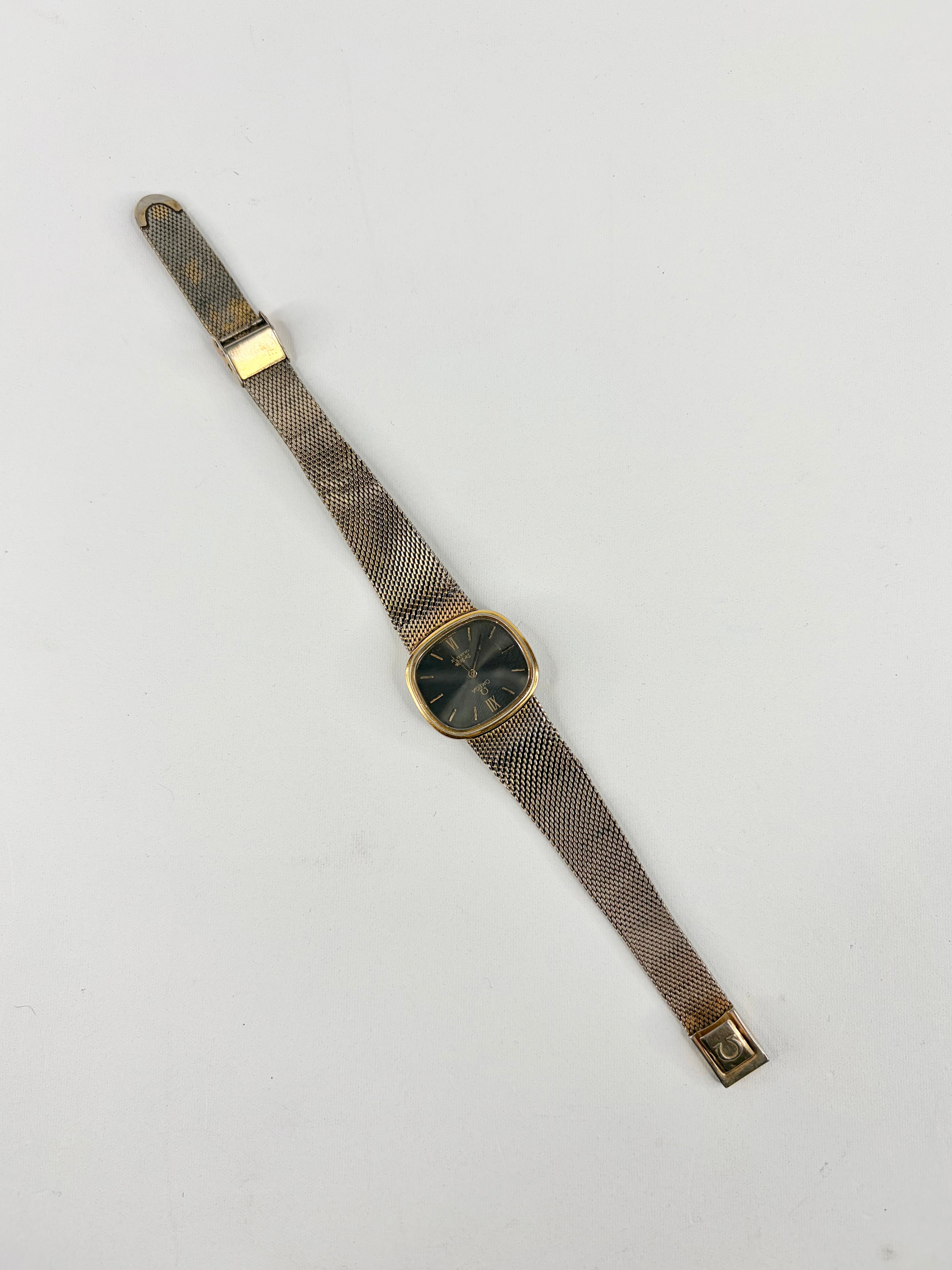 Vintage watch with a gold case and mesh band on a light gray background
