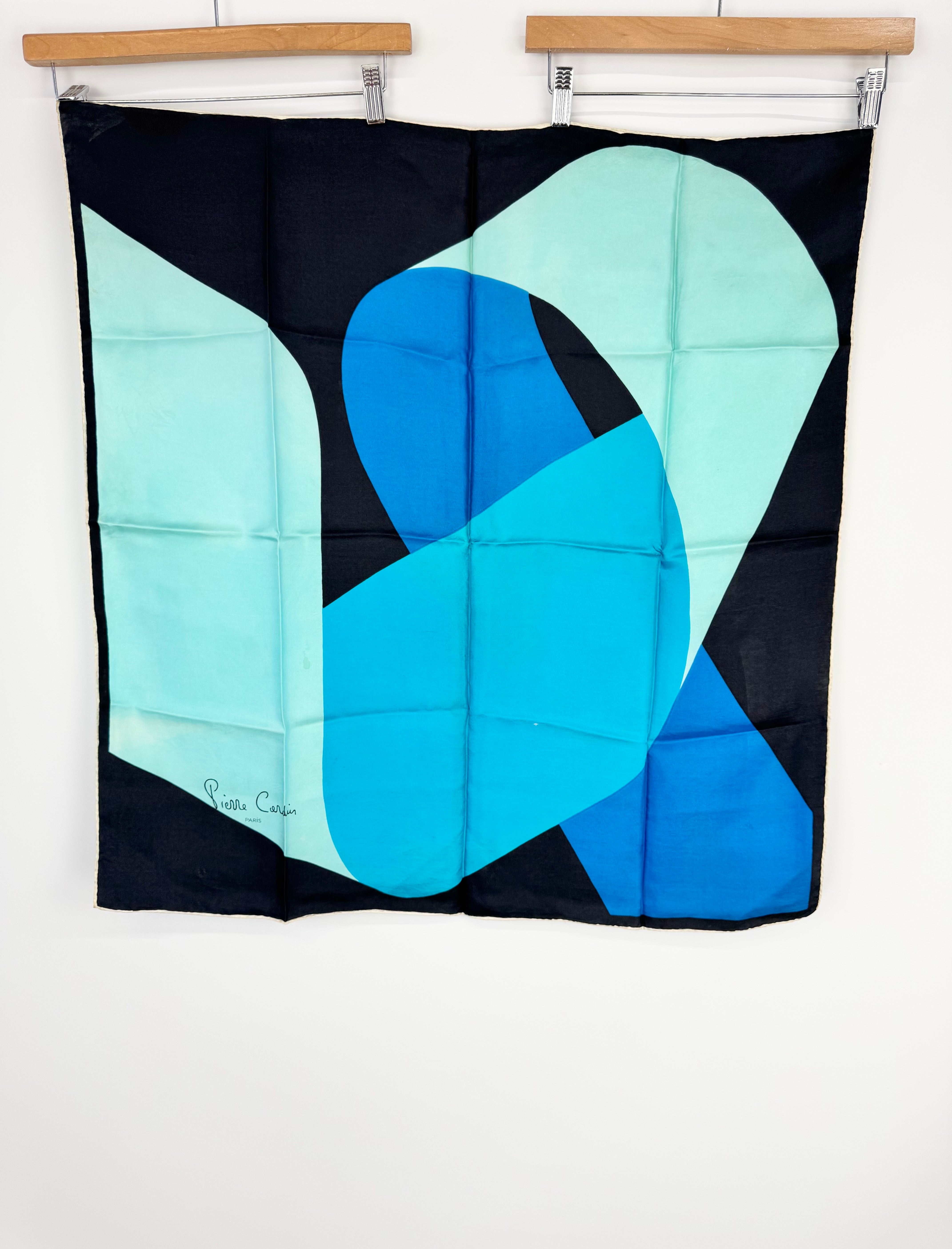 Abstract quilt with blue and green shapes on a black background, hanging on a wall.
