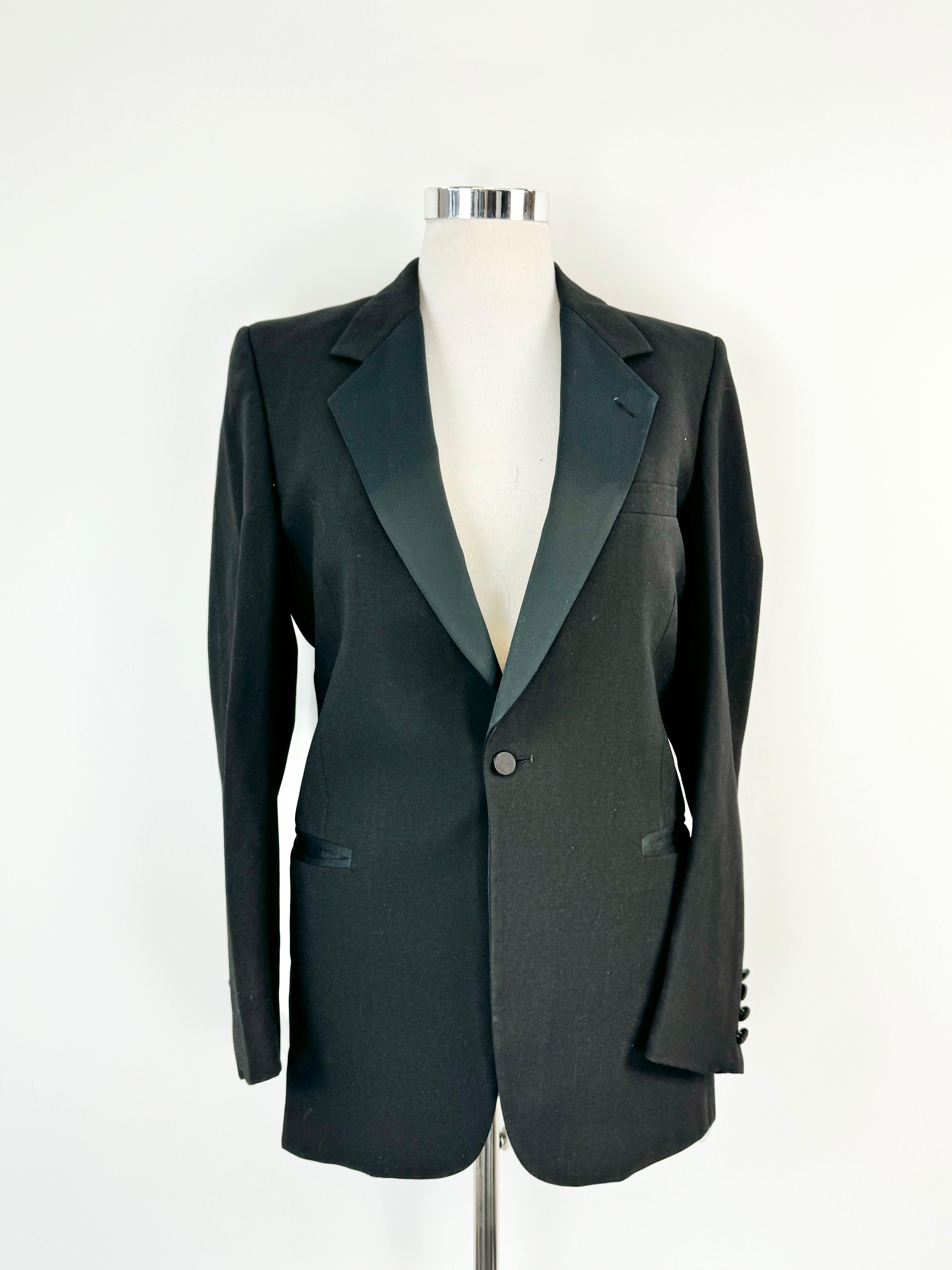 Vintage black Pierre Cardin blazer on a mannequin, showing a fitted silhouette with satin fabric collar and lapel, single fastening at the waist, and two pockets.