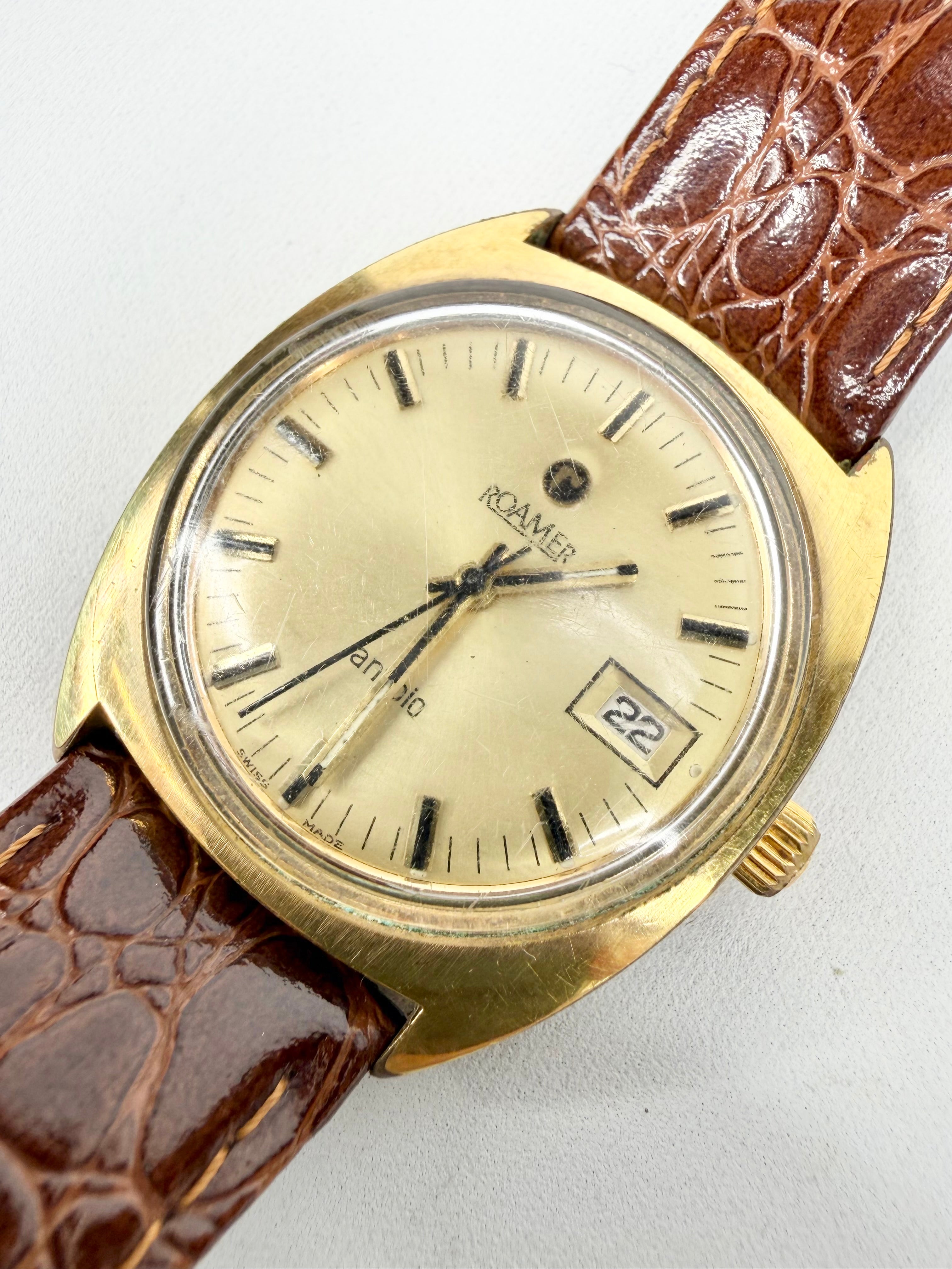 Vintage watch with gold case and brown leather strap on a light gray background