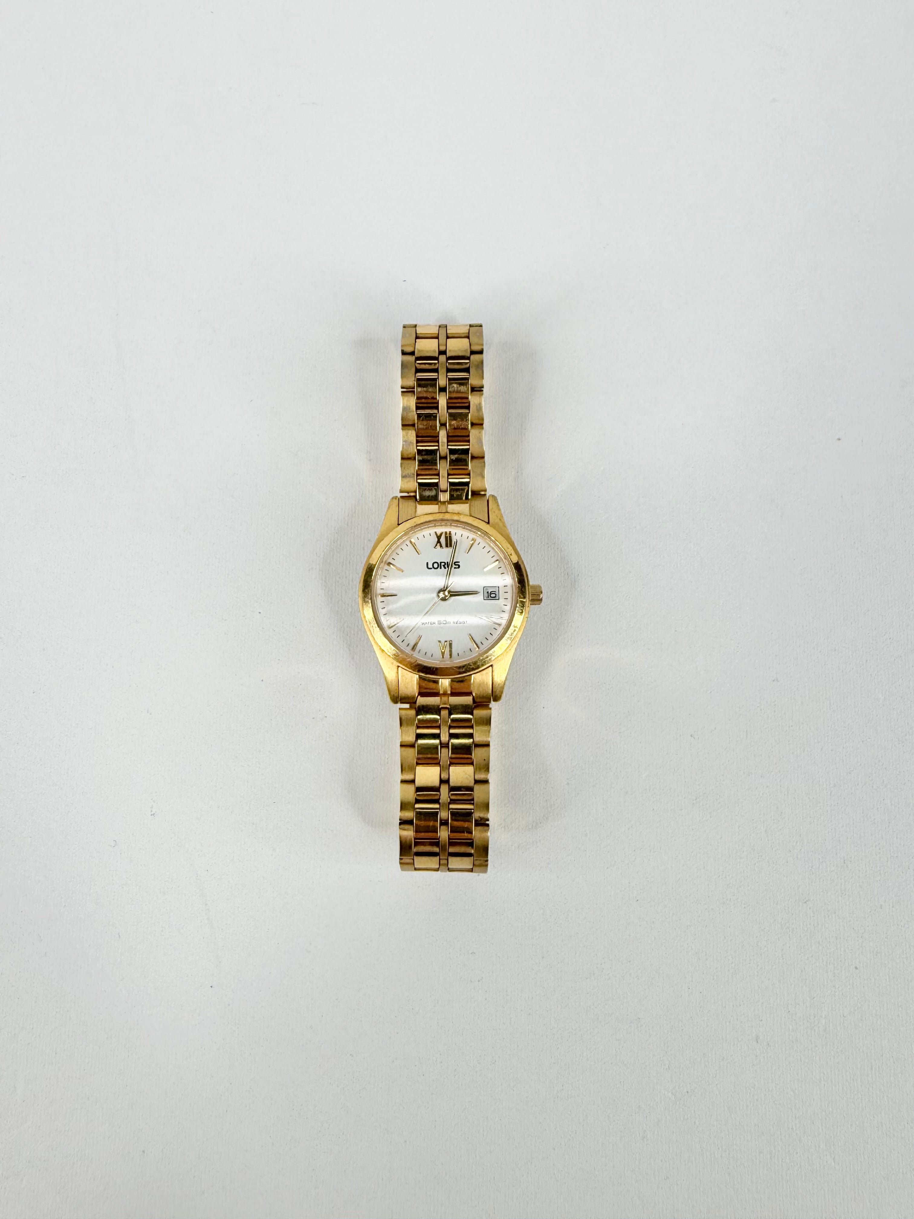 Gold wristwatch with a white face on a light gray background