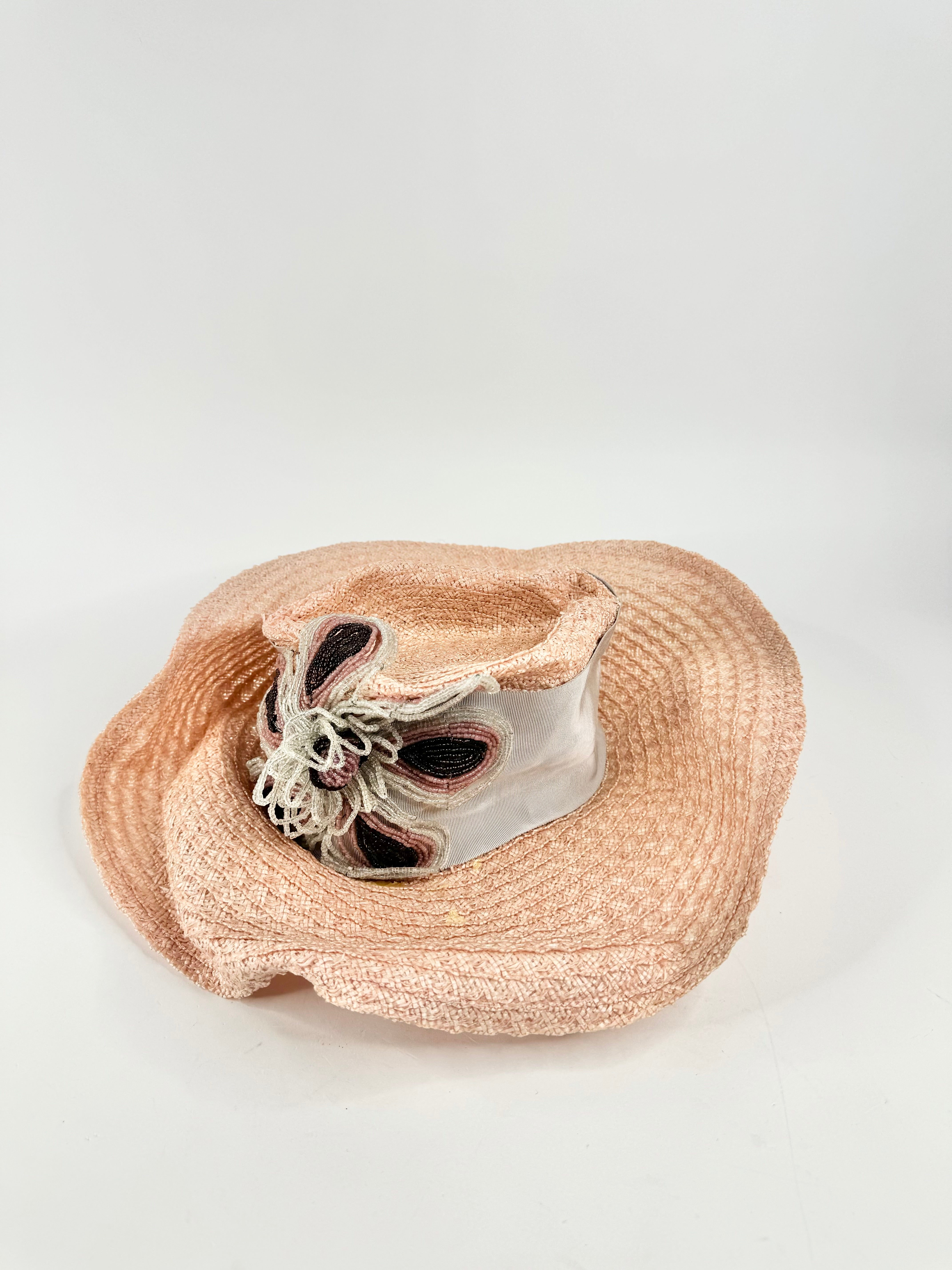 A blush pink woven hat with a large grey ribbon around the brim and a beaded flower embellishment.