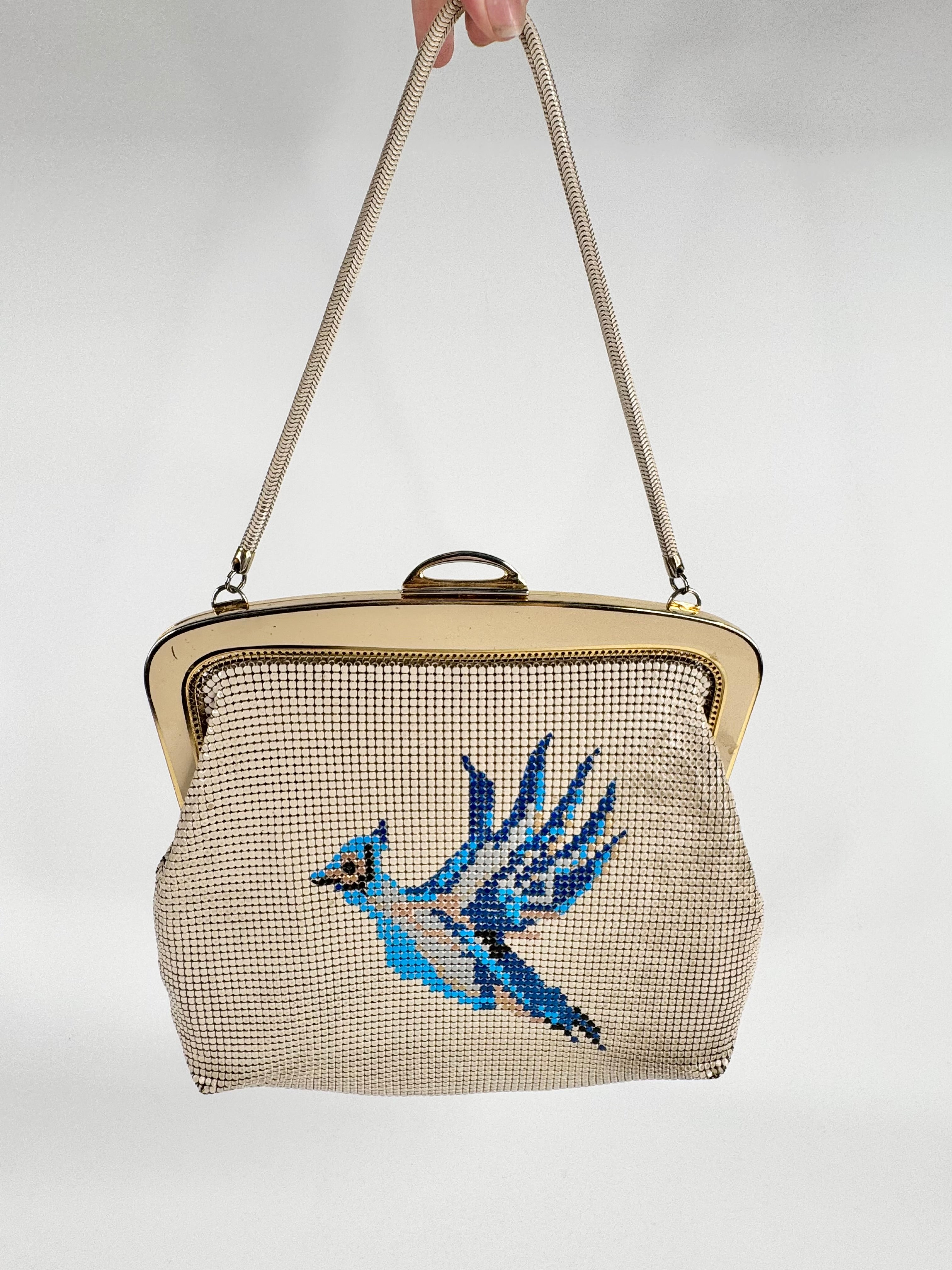 Vintage handbag with mesh design and blue bird embroidery on a white background