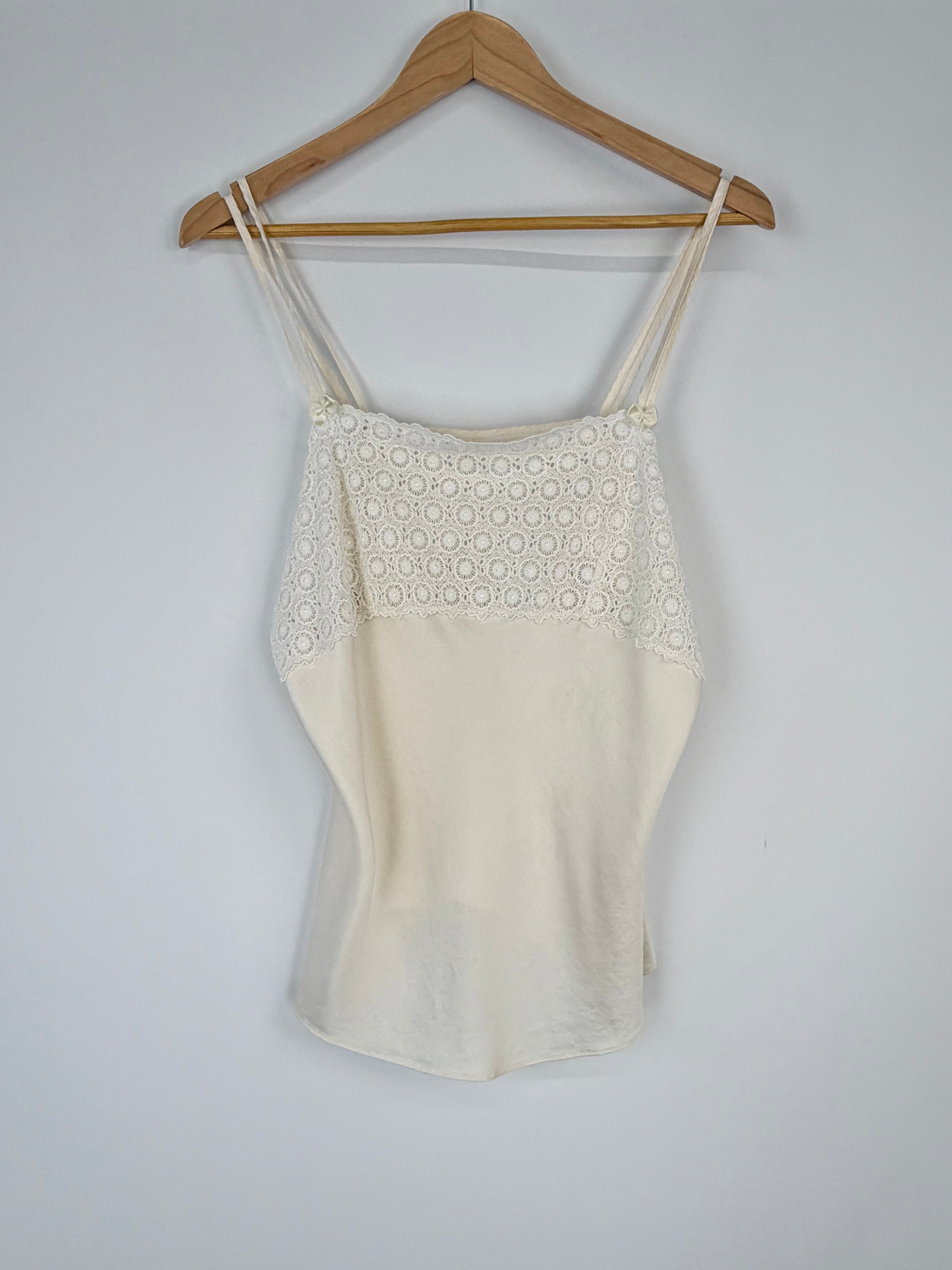 Beige tank top with floral lace details on a wooden hanger against a white background