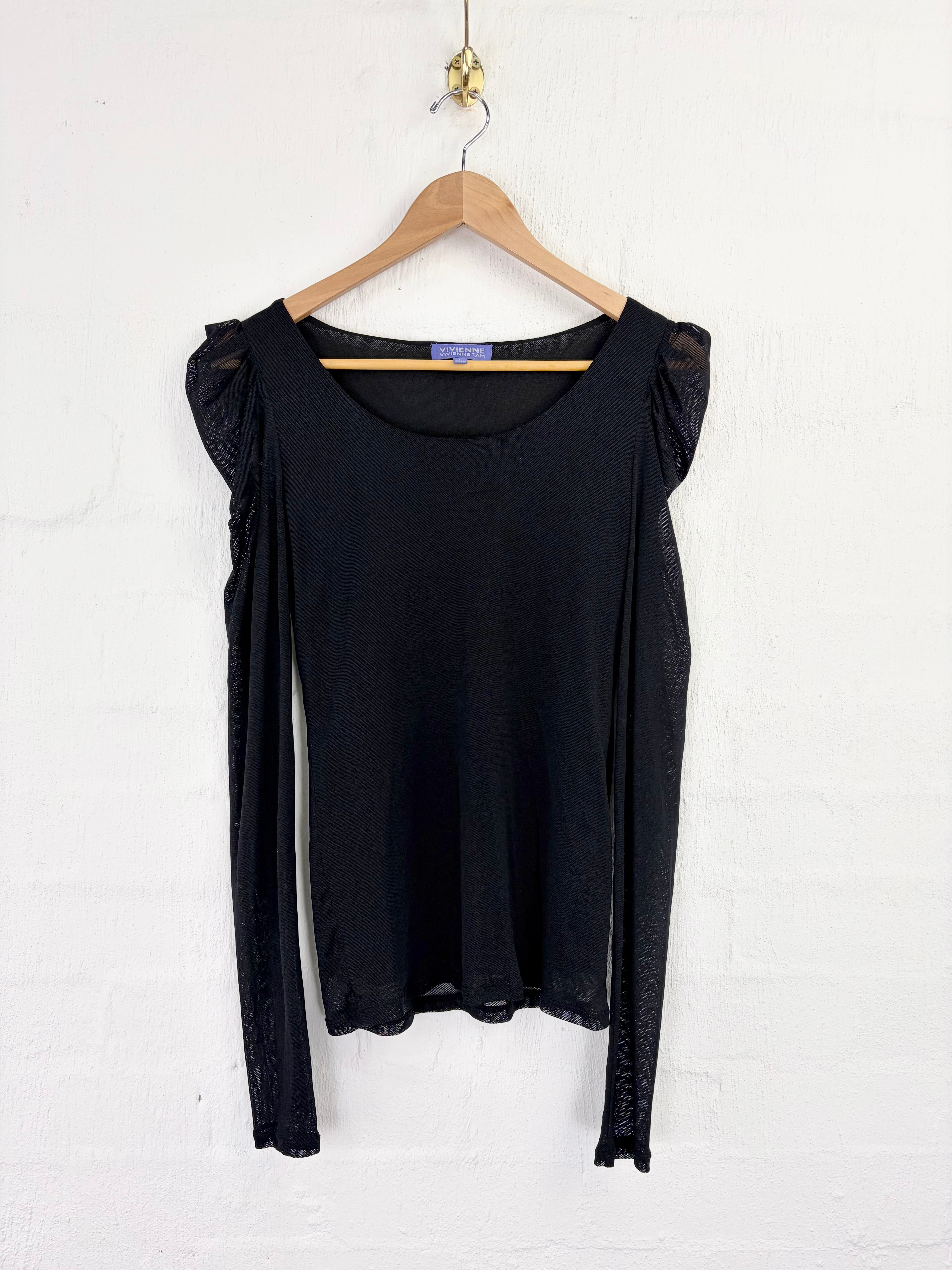 A black long-sleeve blouse with sheer flutter sleeves and a scalloped hem, hanging on a wooden hanger against a white painted brick wall.