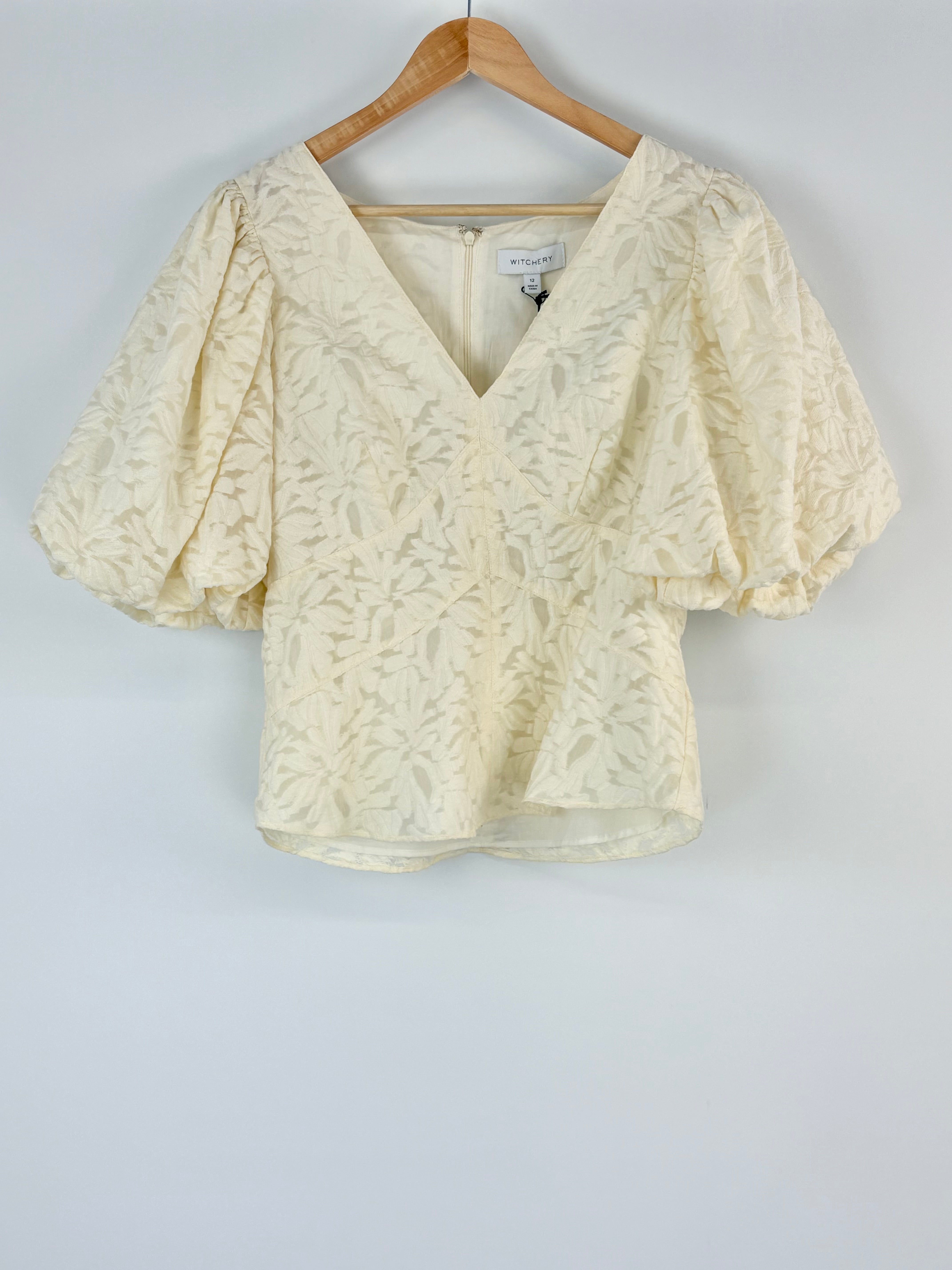 Cream-colored lace top on a wooden hanger against a light gray background