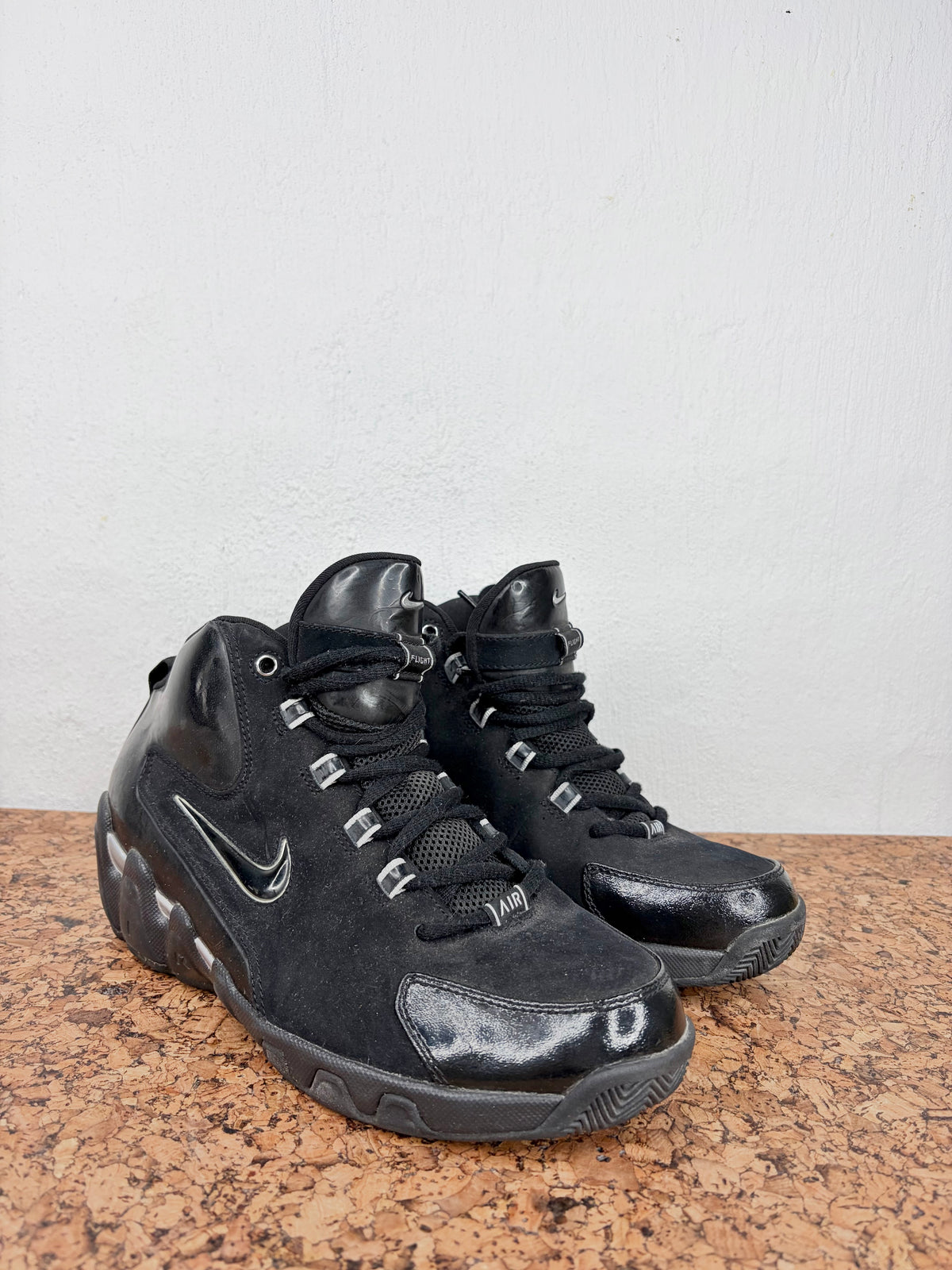 A pair of black Nike high-top sneakers with silver metallic accents, displayed on a brown speckled countertop against a white wall.