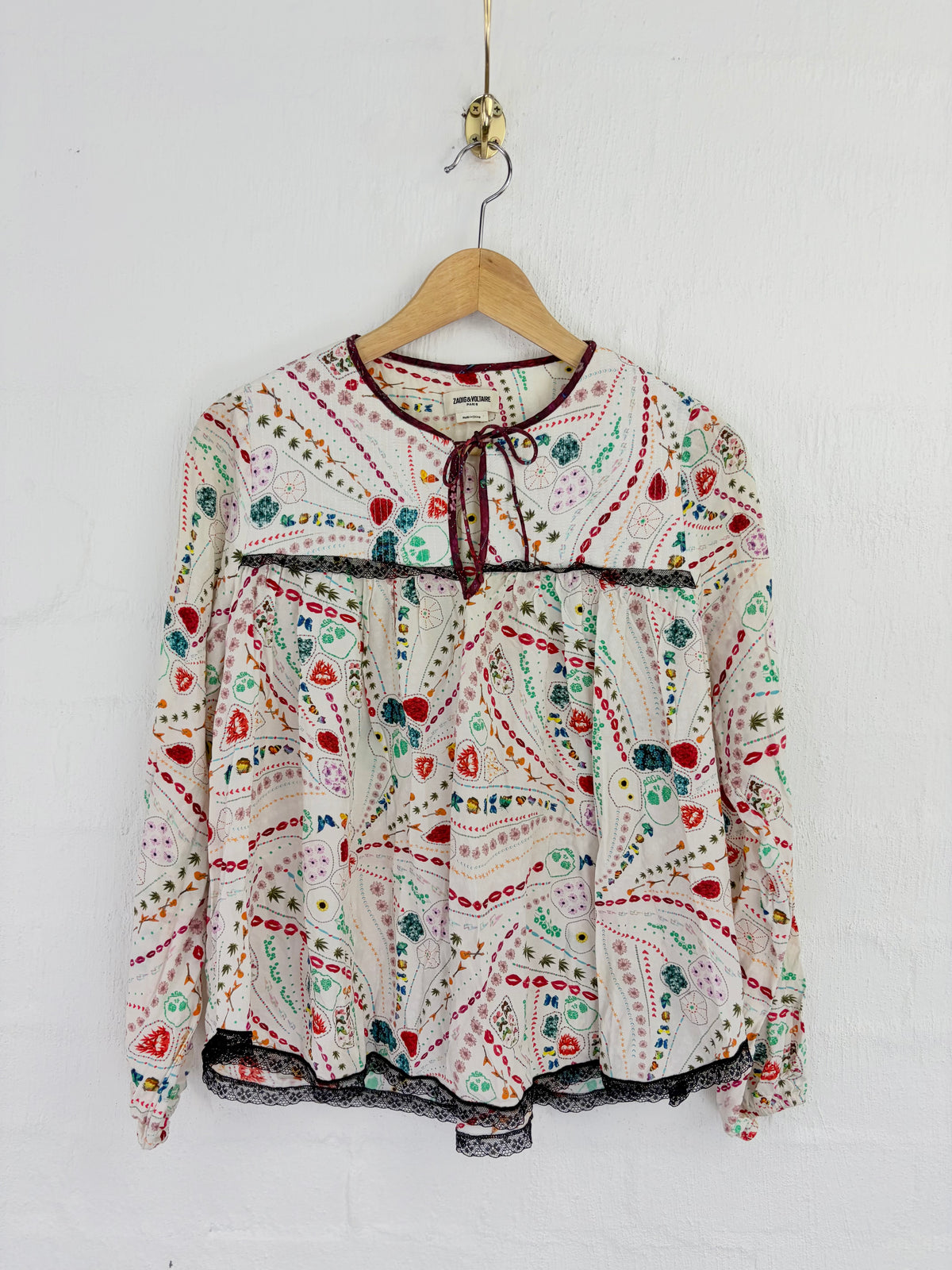 A long-sleeve blouse with a colorful paisley and floral print, hanging on a wooden hanger against a white wall.