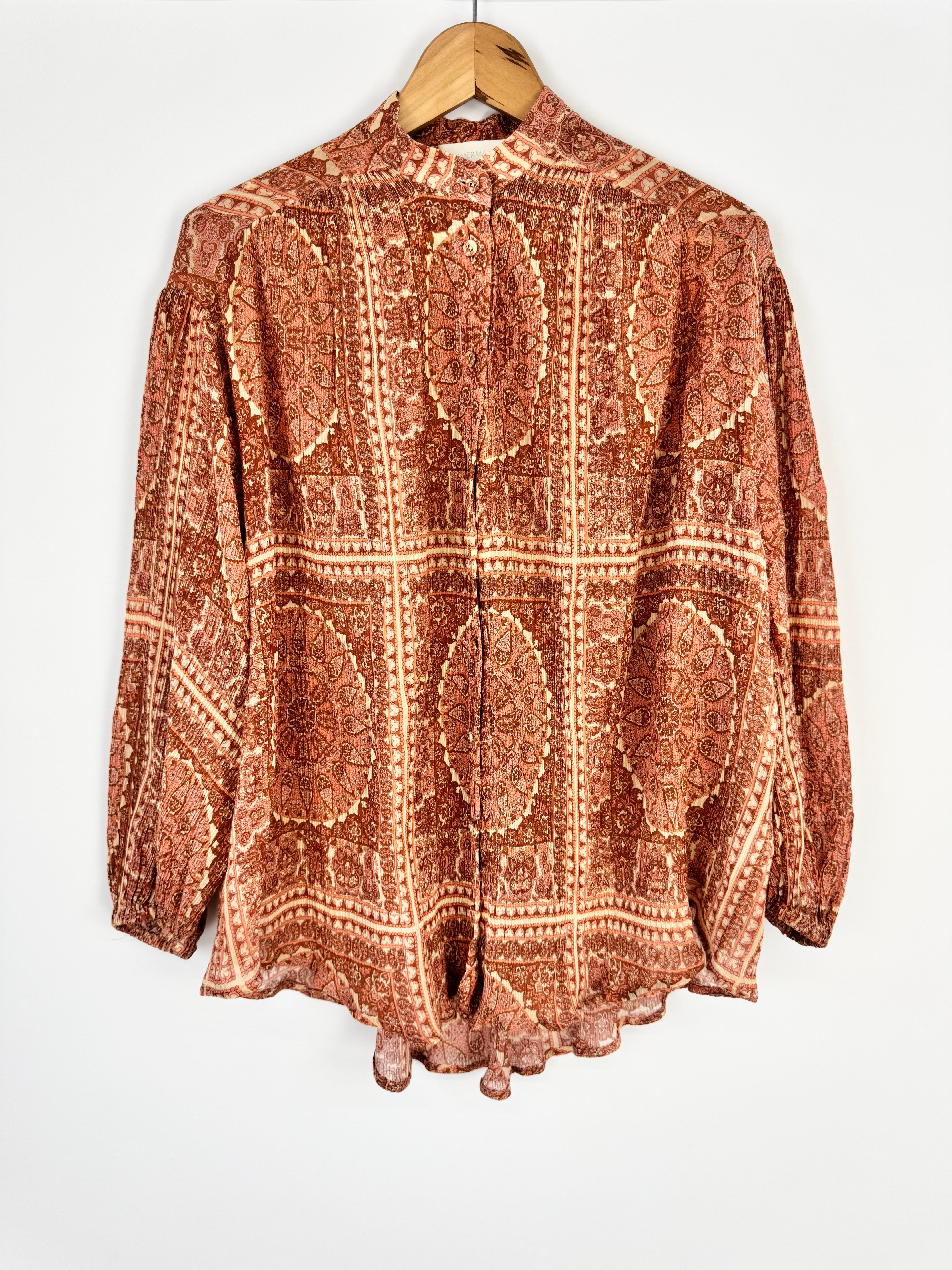 Brown patterned blouse on a wooden hanger against a white background