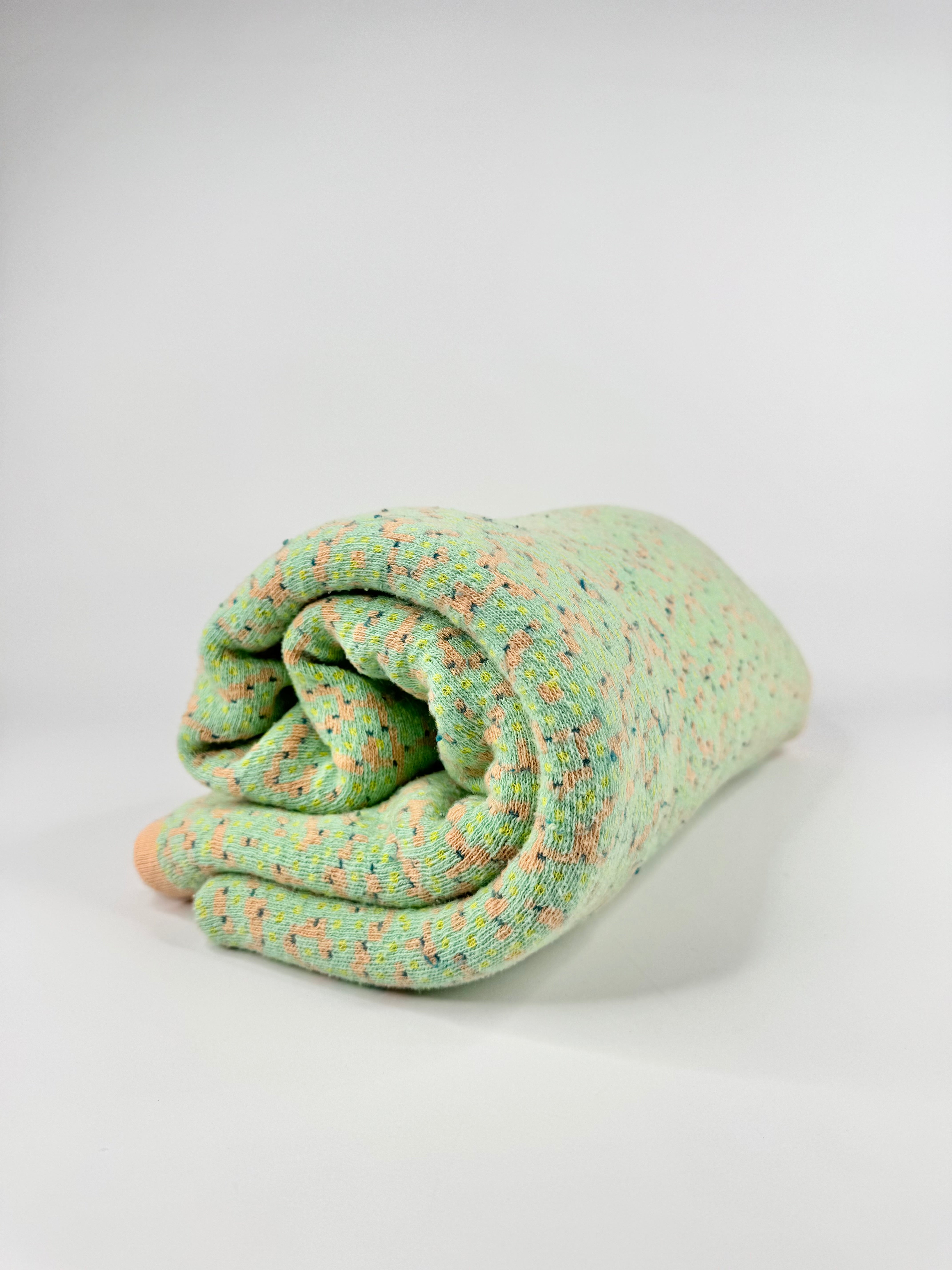 Rolled-up green blanket with small patterns on a white background
